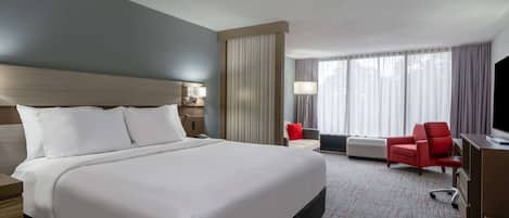 A hotel room with a large bed, a desk, a chair, and a TV.
