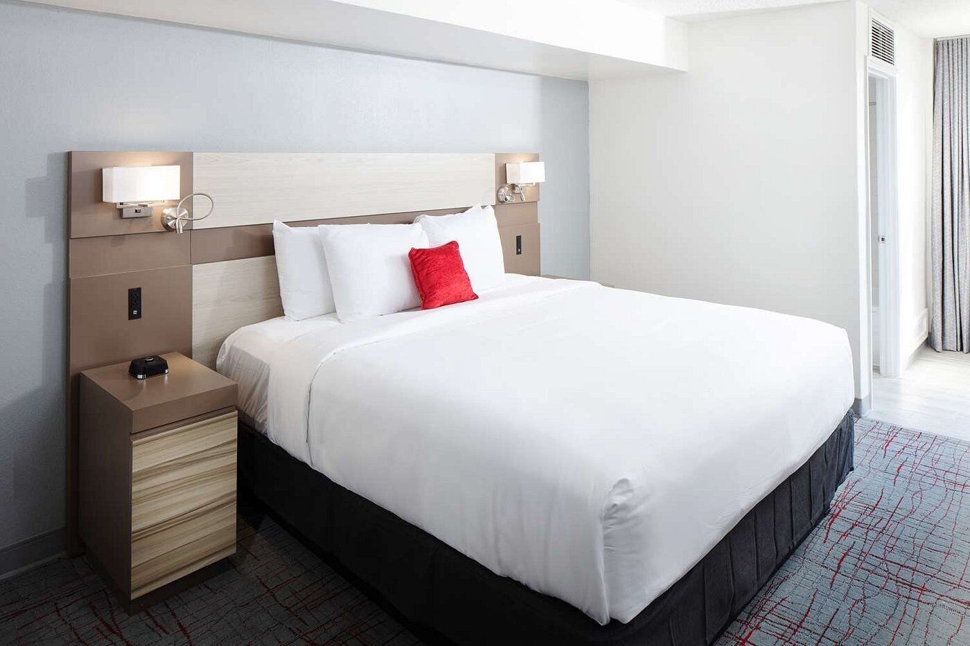 A hotel room with a large bed, a bedside table with a lamp, and a headboard with built-in lighting.