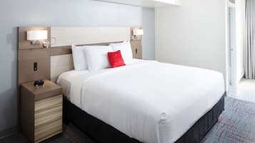 A hotel room with a large bed, a bedside table with a lamp, and a headboard with built-in lighting.