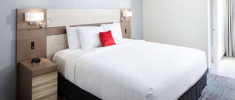 A hotel room with a large bed, a bedside table with a lamp, and a headboard with built-in lighting.