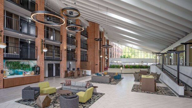A spacious lobby with multiple seating areas, a reception desk, and a large window providing natural light.
