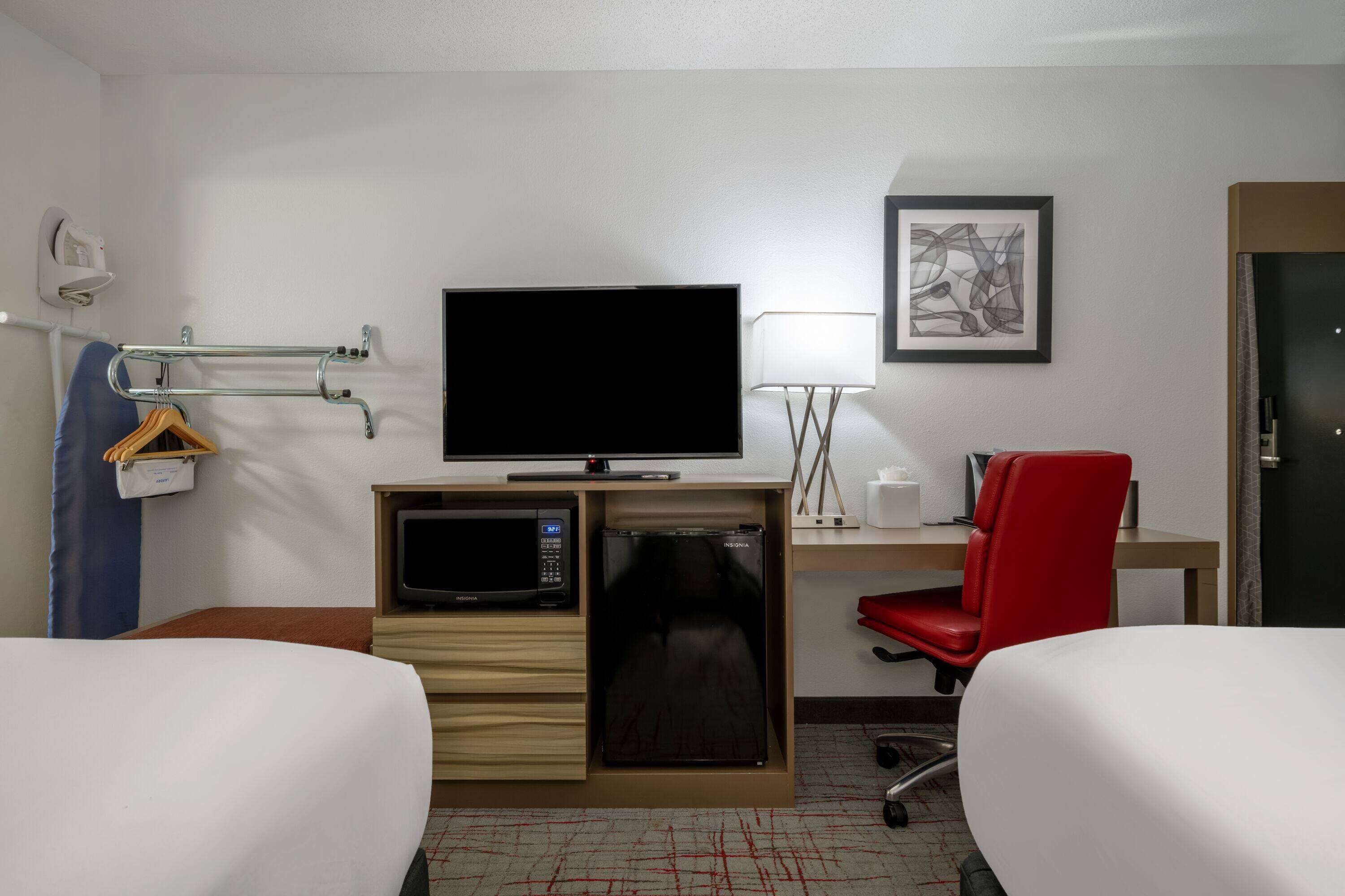 A hotel room with two beds, a television, a microwave, a desk with a chair, and a framed picture on the wall.