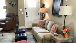 A living room with a brown leather sofa, a beige sofa with patterned cushions, a red armchair, and a wooden coffee table. - High End Townhouse 12 min walk to Campus and Downtown (Auburn)
