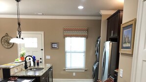 A kitchen with a central island, a dining area with a chair, and a hallway leading to a door. - High End Townhouse 12 min walk to Campus and Downtown (Auburn)