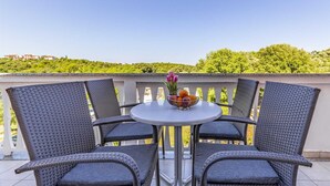 A balcony with wicker chairs and a table, a bowl of fruit, and a vase of flowers.