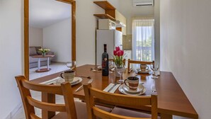 A dining area with a wooden table set for four, a bottle of wine, and a vase with flowers.