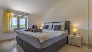 A bedroom with a large bed, a nightstand, a lamp, and a window with curtains.