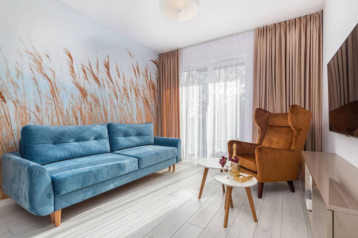 A modern living room with a blue sofa, a brown armchair, and a small round table with a bottle and grapes.