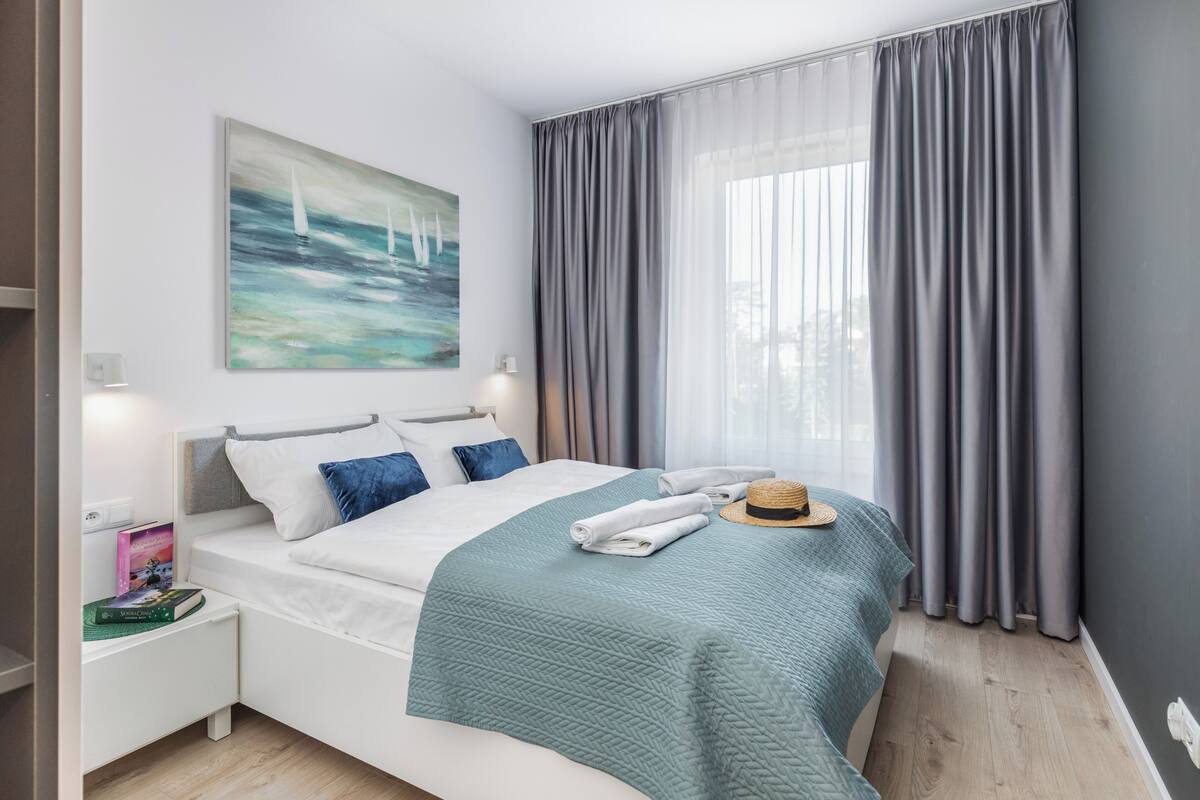 A neatly made bed with a teal blanket, a hat, and folded towels on a white nightstand with books.