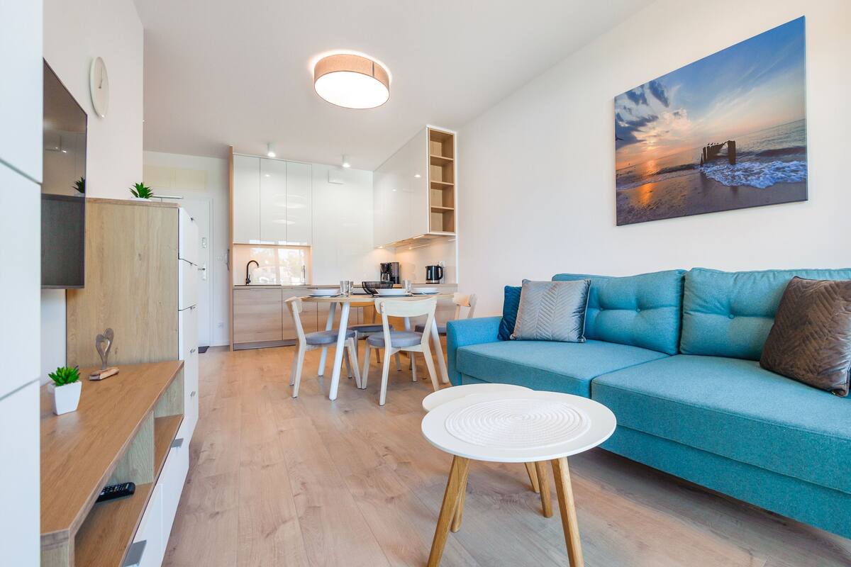 A modern living room with a teal sofa, a white coffee table, and a painting of a beach scene.