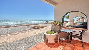 Un balcón con vista al océano, una mesa con sillas y una maceta grande con plantas.