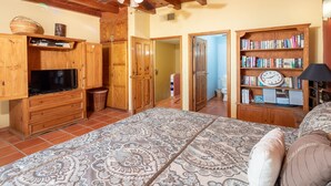 Un dormitorio con cama, armario de madera, televisor, estantería y una alfombra estampada.