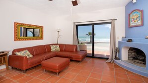 Una sala de estar con un sofá de cuero marrón, una chimenea y vista a la playa.