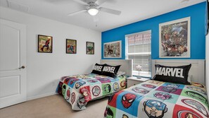 Camera da letto con due letti, pareti blu e biancheria a tema supereroi.