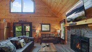 A cozy log cabin interior with a stone fireplace, a large TV mounted above it, and a comfortable seating area with a sofa and a coffee table. - Bootlegger Cabin | Hot Tub | NERF Wall | Arcade (Sevierville)