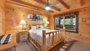 A wooden cabin bedroom with a bed, nightstands, a ceiling fan, and a window with blinds. - Bootlegger Cabin | Hot Tub | NERF Wall | Arcade (Sevierville)