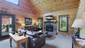 A cozy log cabin interior with a stone fireplace, leather sofas, and a television. - Bootlegger Cabin | Hot Tub | NERF Wall | Arcade (Sevierville)