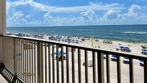 Une vue sur la plage depuis un balcon doté d’une balustrade, avec des parasols de plage et des personnes sur le sable.