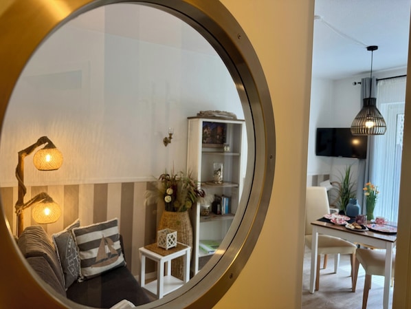 A round mirror reflecting a living room with a sofa, a lamp, and a bookshelf.