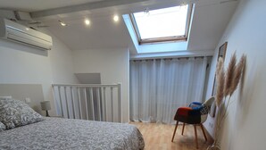 A bedroom with a large bed, a skylight, a chair, and a mirror. - Apartment (Caux)