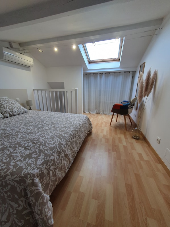 Quarto com uma cama grande, claraboia, cadeira e espelho.
