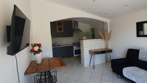 A modern living space with a kitchen, dining area, and a black sofa. - Apartment (Caux)