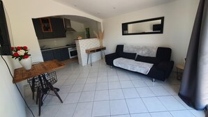 A modern living room with a black sofa, a white coffee table, and a dining area with a wooden table and chairs. - Apartment (Caux)