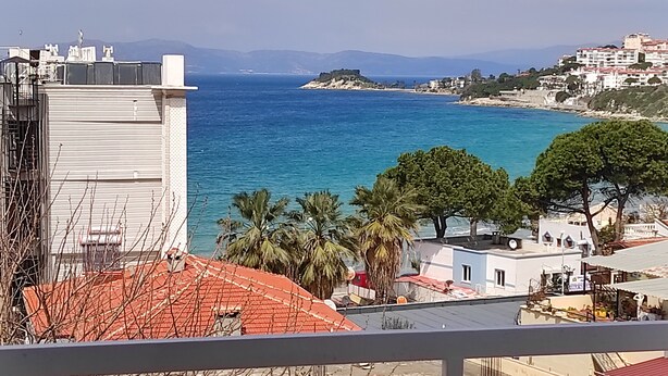 A coastal view with buildings, a beach, and a mountain range in the background. - Afrodit Beach Otel (Kusadasi)