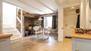 A spacious living area with a stone wall, a dining table with chairs, and a staircase leading to another level. - Awelfa (Newport)