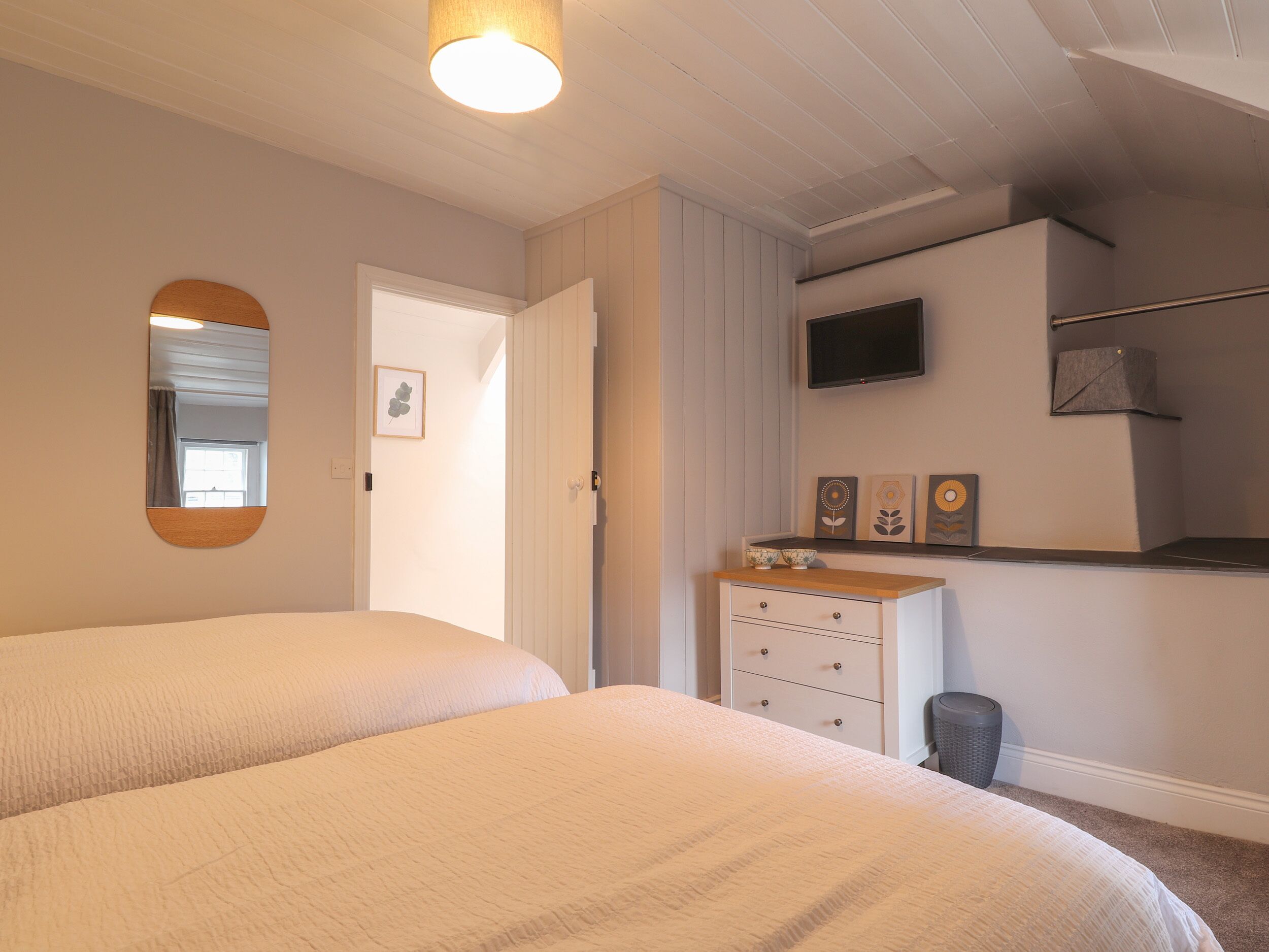 A bedroom with two beds, a dresser, a television, and a door leading to another room.