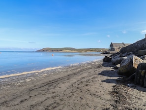 A coastal beach with a rocky shoreline, a clear blue sky, and a distant building. - Awelfa (Newport)