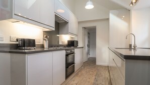A modern kitchen with white cabinetry, a built-in oven, a microwave, and a stainless steel range hood. - Awelfa (Newport)