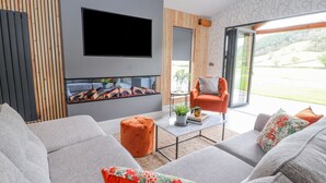 A modern living room with a large flat-screen TV, a fireplace, and a comfortable seating area with sofas and a coffee table. - Pool View (Meifod)