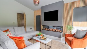 A modern living room with a grey sofa, orange armchair, and a coffee table with a book. - Pool View (Meifod)