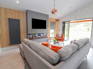 A modern living room with a large grey sectional sofa, a flat-screen TV mounted on the wall, and a glass coffee table. - Pool View (Meifod)
