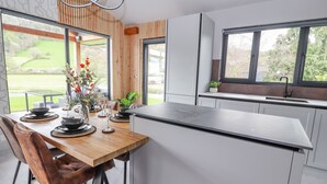 A modern kitchen with a central island, wooden accents, and large windows offering a view of the outdoors. - Pool View (Meifod)