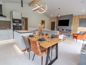 A modern kitchen with an integrated oven and a dining area with a wooden table and chairs. - Pool View (Meifod)