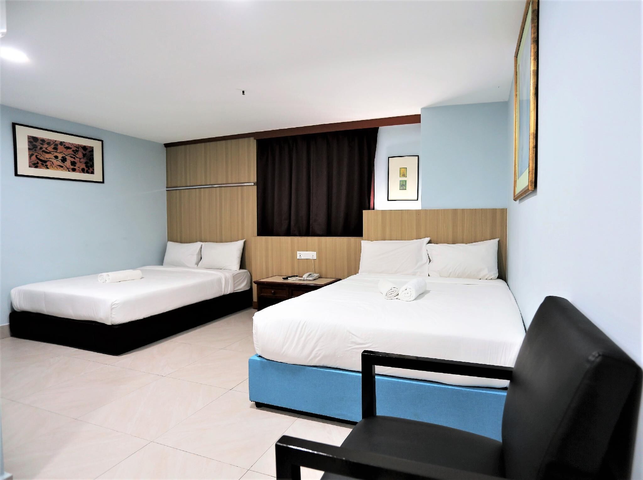 A hotel room with two single beds, a desk with a chair, and a large window with curtains.
