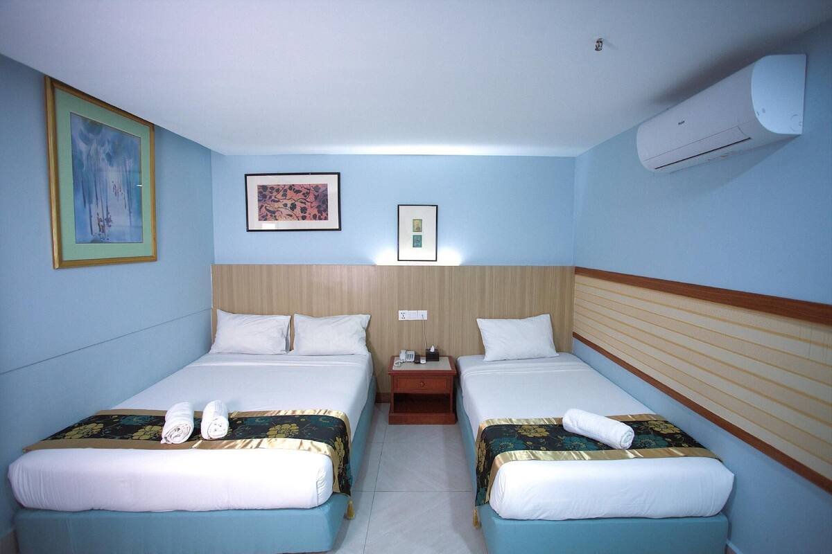 Habitación de hotel con dos camas, una mesita de noche y un equipo de aire acondicionado.