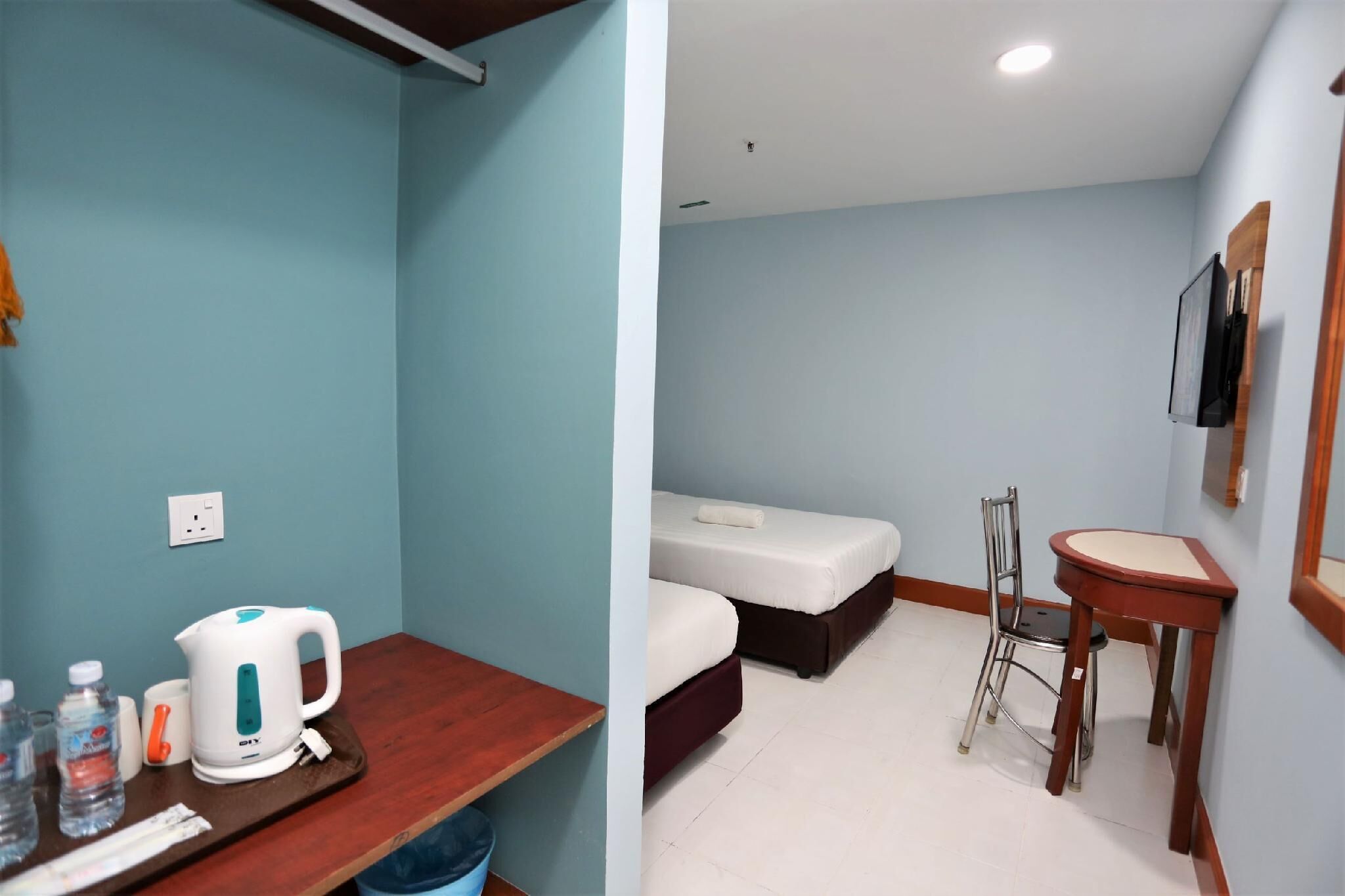 A room with a bed, a chair, a table, a kettle, and a TV.