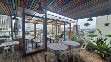 An outdoor dining area with tables and chairs, a wooden deck, and a view of the cityscape.