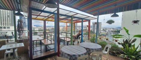 Un área de comedor al aire libre con mesas y sillas, una terraza de madera y vistas a la ciudad.