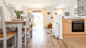 A modern kitchen with wooden cabinets, a built-in oven, and a dining area with a white table and chairs. - Charleston Cottage (Falmouth)