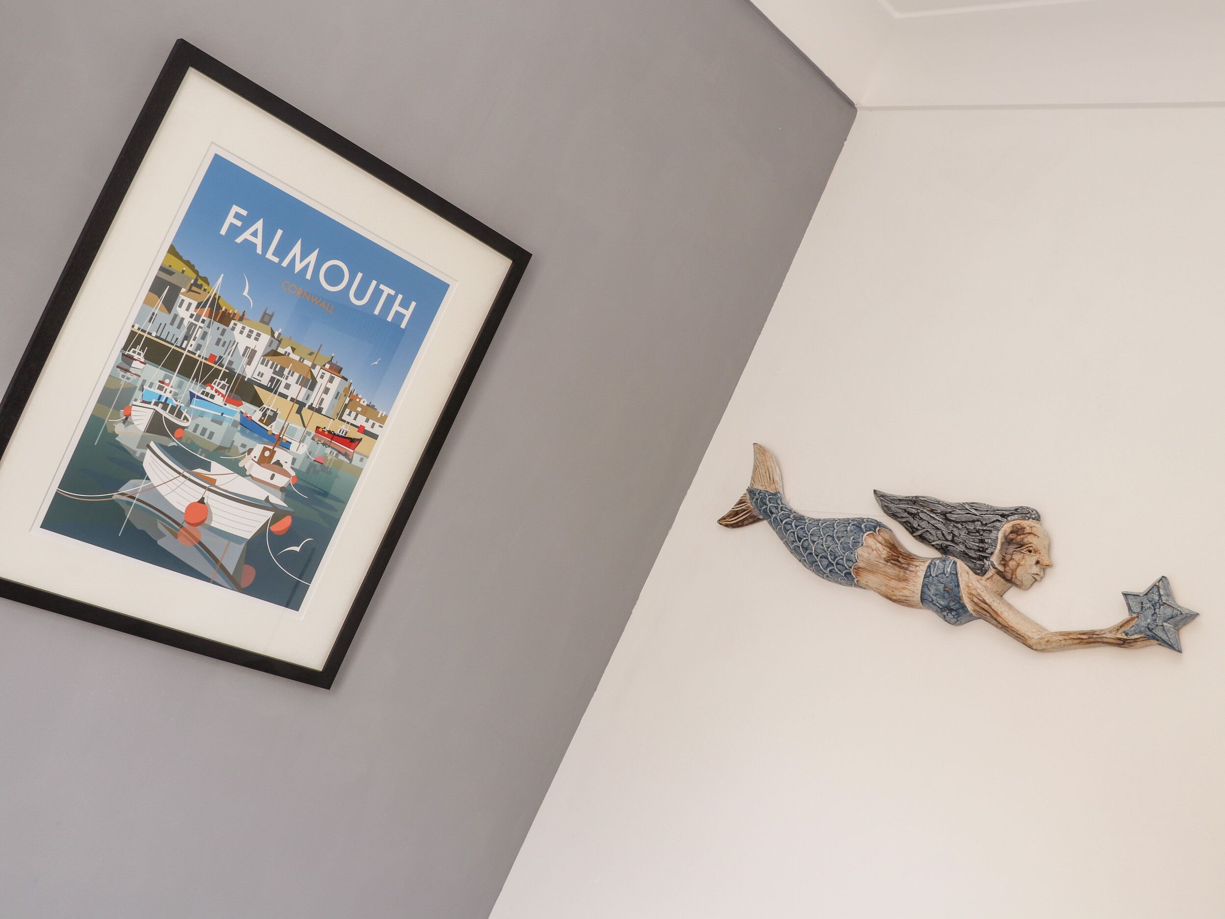 A framed picture of Falmouth with a harbor scene and a wooden sculpture of a mermaid.