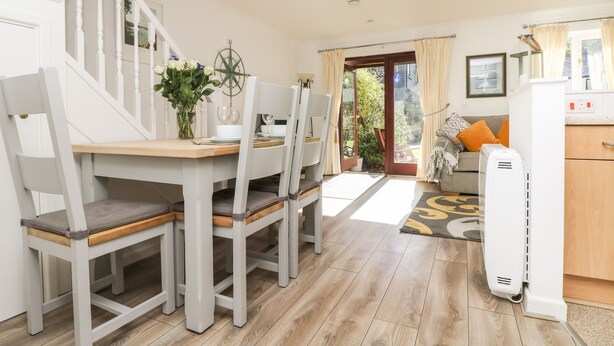 A dining area with a wooden table and chairs, a vase of flowers, and a view of the garden through the open door. - Charleston Cottage (Falmouth)