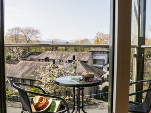 A balcony with a table, chairs, and a view of traditional buildings and trees.