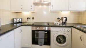 Cocina compacta con armarios blancos, horno integrado, lavadora, tostadora y hervidor.