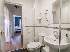 A bathroom with a toilet, sink, and glass shelves. There is a door leading to another room.