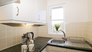 Una cocina con armarios blancos, una ventana, un lavamanos y un hervidor.