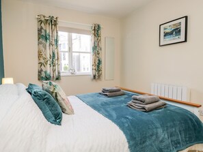 A bedroom with a bed, a window with curtains, a radiator, and a framed picture on the wall.